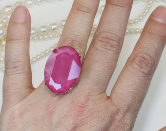 May include: A pink oval-shaped ring with a large faceted gemstone. The ring is worn on a person's finger.