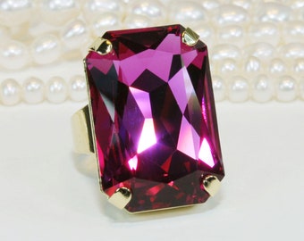 May include: A gold ring with a large, faceted, rectangular, fuchsia-colored gemstone.