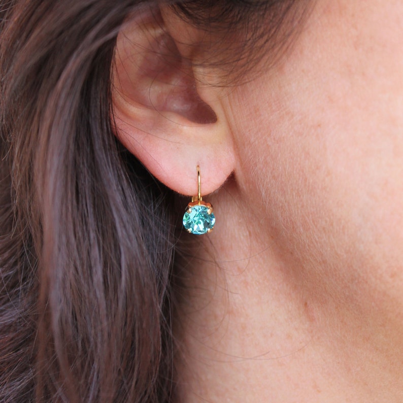 May include: Gold earrings with a light blue gemstone.