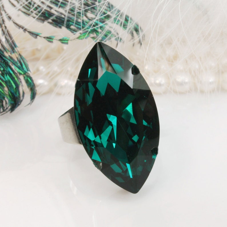 May include: A silver ring with a large, emerald green marquise-shaped crystal.