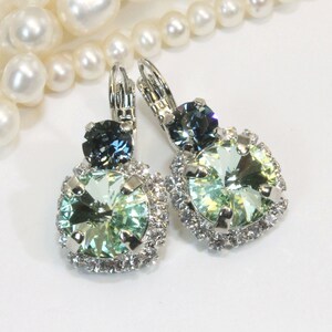 May include: Silver dangle earrings with a large light green crystal surrounded by smaller clear crystals and a smaller dark blue crystal.