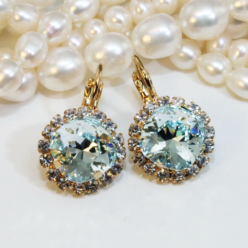 May include: A pair of gold earrings with a light blue crystal surrounded by smaller clear crystals.