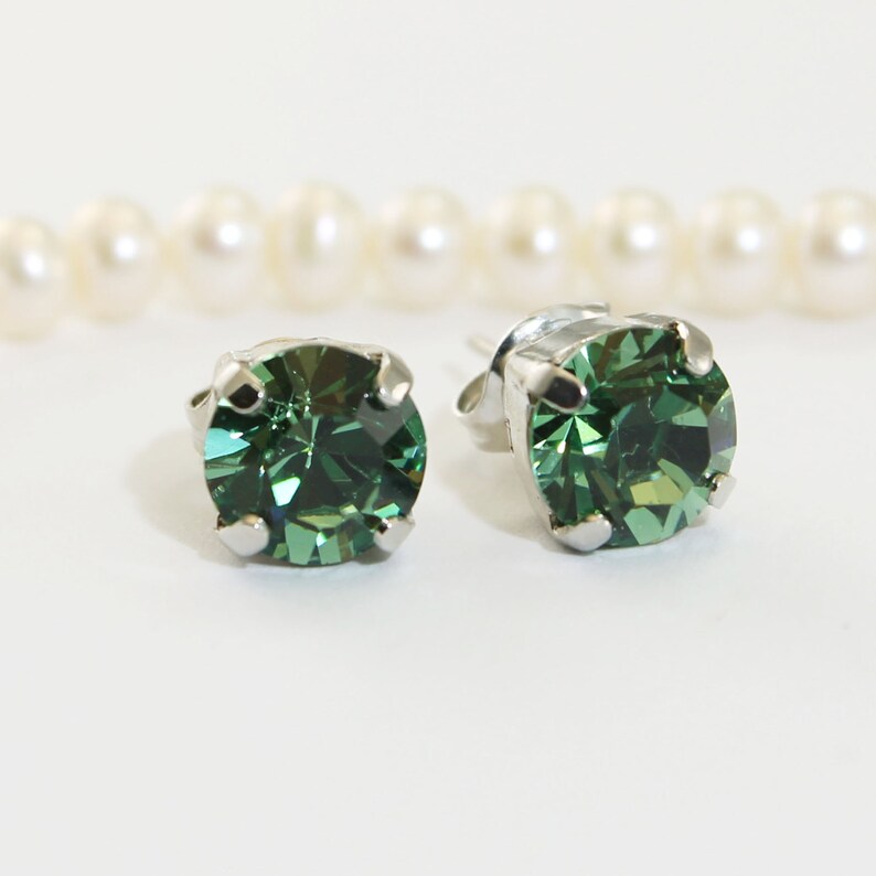 May include: A pair of silver stud earrings with round, green gemstones.