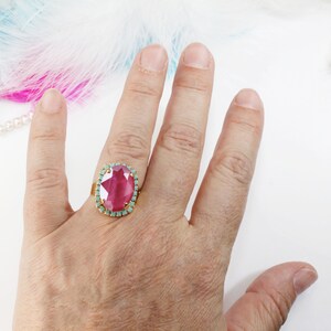 May include: A gold ring with a large oval pink gemstone surrounded by a halo of smaller turquoise gemstones.
