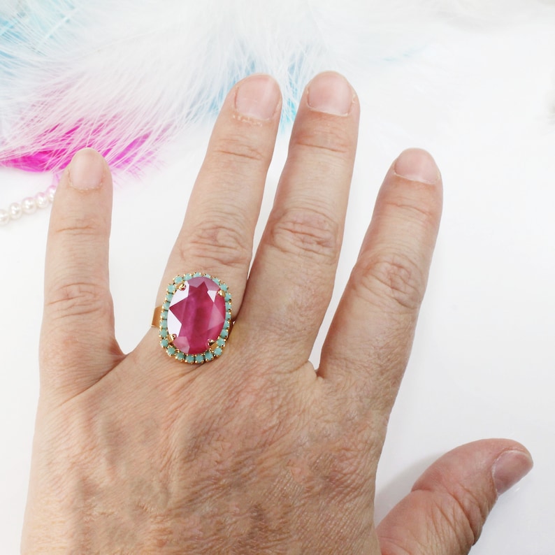 May include: A gold ring with a large oval pink gemstone surrounded by a halo of smaller turquoise gemstones.