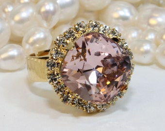 May include: A gold ring with a large, light pink, faceted gemstone surrounded by a halo of clear rhinestones.