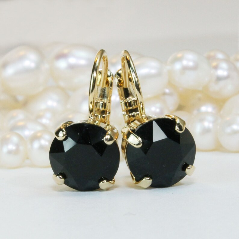 May include: A pair of gold hoop earrings with black crystal stones. The earrings are on a white background with white pearls.