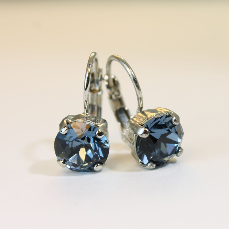 May include: A pair of silver hoop earrings with a blue crystal stone in the center of each hoop.