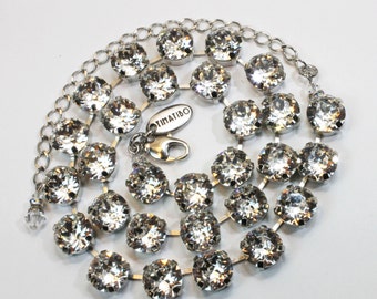 Puede incluir: Un collar de tono plateado que presenta una serie de cristales redondos, transparentes y facetados engarzados en metal. El collar incluye un cierre de mosquetón, una cadena ajustable y una pequeña etiqueta ovalada grabada con TIMATIBO.