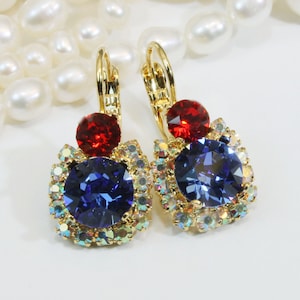 Könnte beinhalten: Goldene Ohrhänger mit einem blauen und roten Kristalldesign. Die Ohrringe haben einen großen blauen Kristall, der von kleineren klaren Kristallen umgeben ist, und einen kleineren roten Kristall oben.