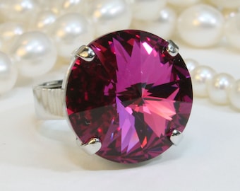 May include: A silver ring with a large, round, faceted, fuchsia-colored gemstone.