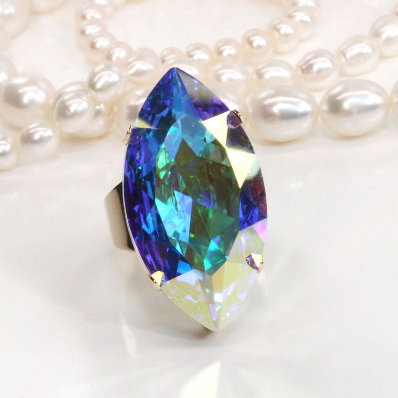 May include: A large, faceted, iridescent blue and green gemstone ring with a marquise cut. The ring is set in a silver band.