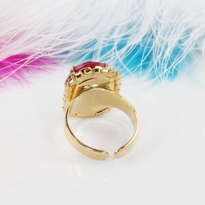 May include: A gold ring with a large, red, oval-shaped gemstone set in a gold bezel. The ring is adjustable and has a simple, classic design.
