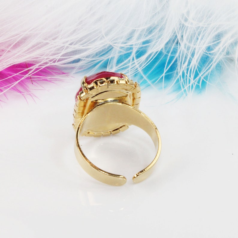 May include: A gold ring with a large, red, oval-shaped gemstone set in a gold bezel. The ring is adjustable and has a simple, classic design.