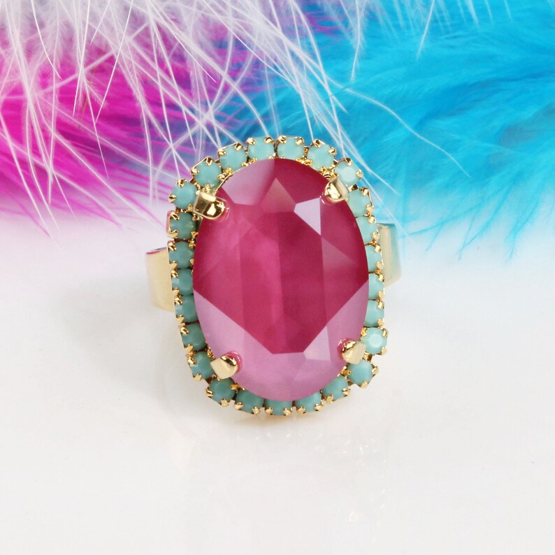 May include: A gold ring with a large oval pink gemstone surrounded by a ring of light blue rhinestones.