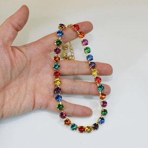 Puede incluir: Un collar de cadena dorada con piedras redondas de color arco&iacute;ris. El collar est&aacute; en una mano.