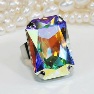May include: A silver ring with a large, rectangular, iridescent gemstone. The gemstone has a rainbow of colors, including purple, blue, green, yellow, and orange.