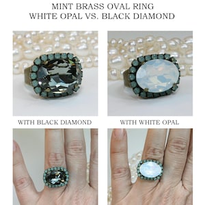 May include: An oval brass ring featuring a large central stone surrounded by small mint-colored crystals. The design is available with either a dark black diamond-colored stone or a milky white opal-colored stone, both set in a vintage-style brass band.