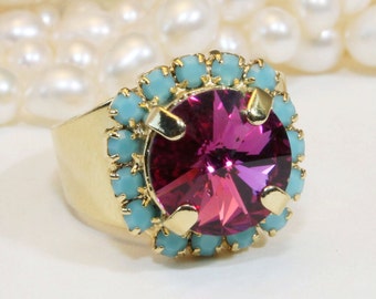 May include: A gold ring with a large, round, fuchsia-colored gemstone surrounded by a halo of smaller, turquoise-colored gemstones.