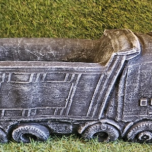 May include: A grey concrete planter shaped like a dumper truck. The planter has a weathered look and is ideal for adding a rustic touch to your garden.