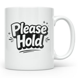 以下が含まれることがあります： 「Please Hold」の文字が黒色の太字でスタイリッシュに描かれた白いセラミックマグカップ。マグカップにはカーブした取っ手があり、白い背景に配置されています。テキストは装飾的なスターバーストで囲まれています。