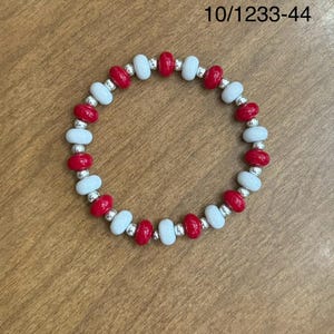 Könnte beinhalten: Ein rot-weißes Perlenarmband mit silbernen Akzenten. Das Armband trägt die Nummer 10/1233-44, die auf dem Hintergrund aufgedruckt ist.