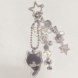 Peut inclure: Un porte-cl&eacute;s en argent avec un charme de personnage de dessin anim&eacute;, un charme d'&eacute;toile et plusieurs autres charmes, dont des n&oelig;uds, des fleurs et des flocons de neige.
