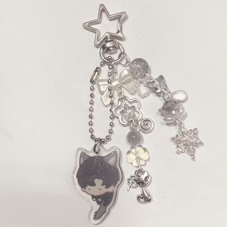 Peut inclure: Un porte-cl&eacute;s en argent avec un charme de personnage de dessin anim&eacute;, un charme d'&eacute;toile et plusieurs autres charmes, dont des n&oelig;uds, des fleurs et des flocons de neige.