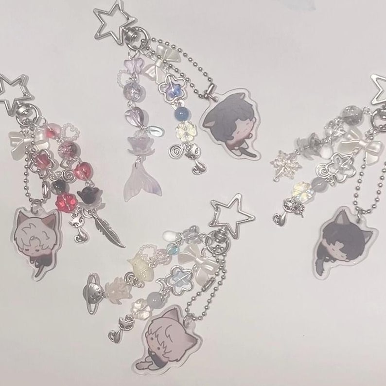 Peut inclure: Quatre colliers &agrave; breloques avec des breloques en forme d'&eacute;toile et diverses perles, breloques et pendentifs. Chaque collier pr&eacute;sente un personnage de dessin anim&eacute; diff&eacute;rent avec des cheveux noirs et des oreilles de chat. Les breloques comprennent des &eacute;toiles, des c&oelig;urs, des fleurs et d'autres &eacute;l&eacute;ments d&eacute;coratifs.