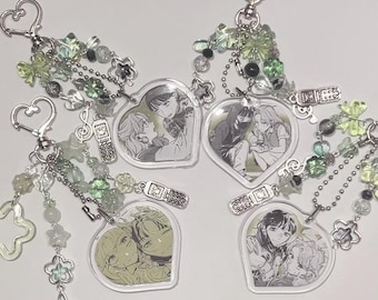 May include: Four heart-shaped keychains with anime character illustrations. Each keychain features a silver chain with green and silver beads and charms.
