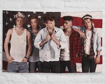 May include: Five young men stand in front of an American flag. They are all wearing casual clothing, including jeans, t-shirts, and jackets. The men are looking at the camera.