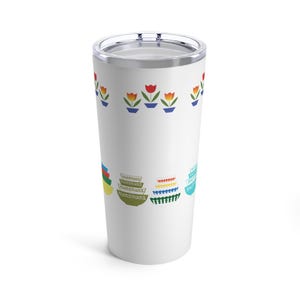 Op de afbeelding: Een witte roestvrijstalen tumbler met een bloemenpatroon en een stapel kleurrijke kommen. Het bloemenpatroon heeft rode tulpen met groene bladeren en blauwe potten. De kommen zijn gestapeld in een regenboogpatroon.