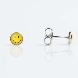 May include: A pair of silver stud earrings with a yellow smiley face design.