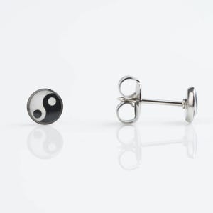 May include: A pair of silver stud earrings with a black and white yin yang symbol design.