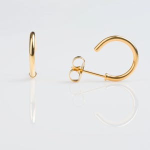 May include: A pair of gold hoop earrings with a simple, minimalist design. The earrings are made of a smooth, polished metal and have a classic, timeless look.
