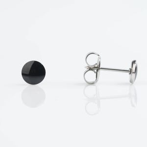 May include: A pair of stud earrings. One earring is a black, circular stud. The other earring is a silver-colored post with a black, circular stud. The earrings are displayed on a white surface.