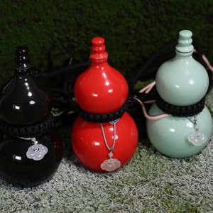 May include: Three gourd-shaped ceramic bottles with black, red, and light green glaze. Each bottle has a black cord tied around the neck and a white jade pendant hanging from the cord.