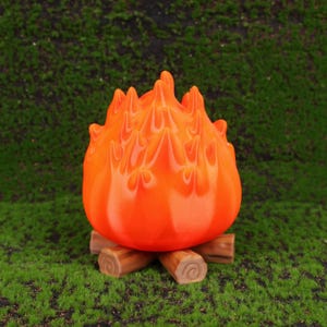 Desktop setup featuring the Fire Demon Calcifer-inspired organizer in a cozy home office environment. The piece is used to store SD cards, USB drives, and earbuds, demonstrating its practical utility while also showcasing its artistic design. With its Studio Ghibli inspiration and compact size, this desk accessory is ideal for anime lovers and collectors looking for functional decor.
