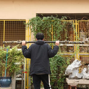 May include: A black staff with ornate, detailed carvings at each end, held by a person. The carvings feature gold and cream colors. The staff is held horizontally across the person's shoulders.