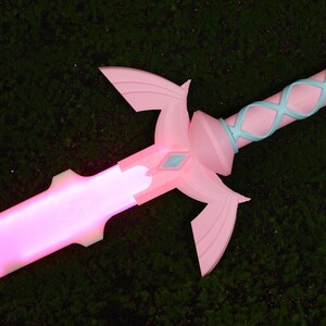 Puede incluir: Una espada de pl&aacute;stico rosa y azul con una hoja que se ilumina. La espada tiene un dise&ntilde;o decorativo en el mango y una gema en forma de diamante en la empu&ntilde;adura.