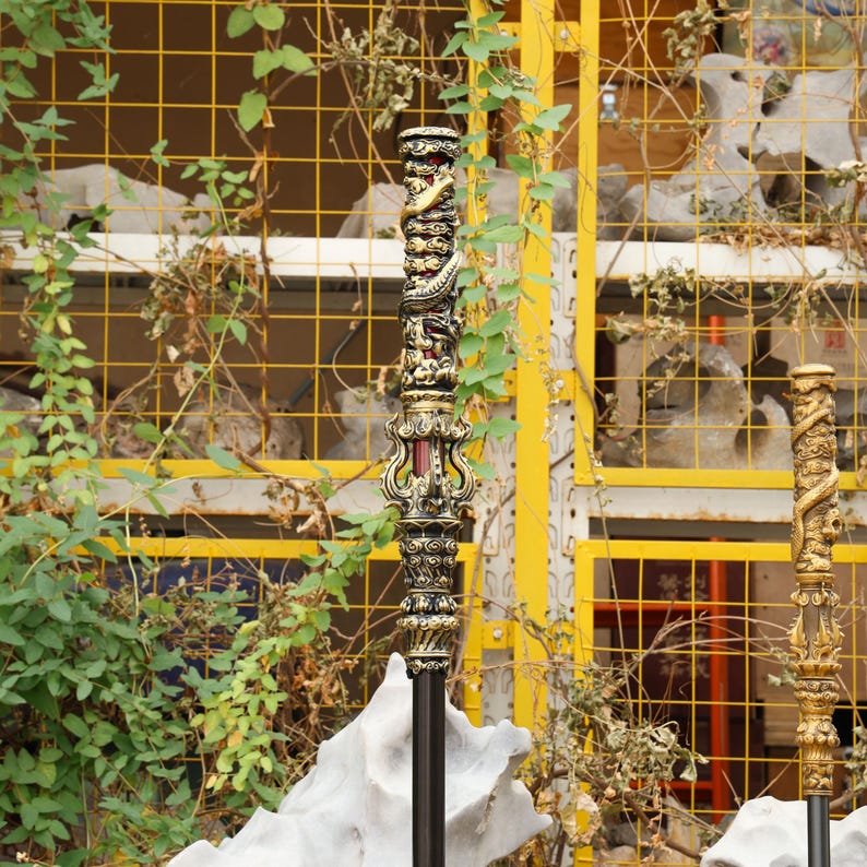 May include: Ornate, dark-colored staff with intricate carvings and gold accents. The staff features a detailed design with a dragon motif and a decorative handle. The staff is set against a backdrop of greenery and a yellow grid.