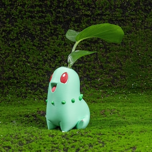 May include: A light green Chikorita planter with red eyes and a smiling mouth, holding a green plant with large leaves. The planter has small green spikes and is set against a backdrop of green moss.