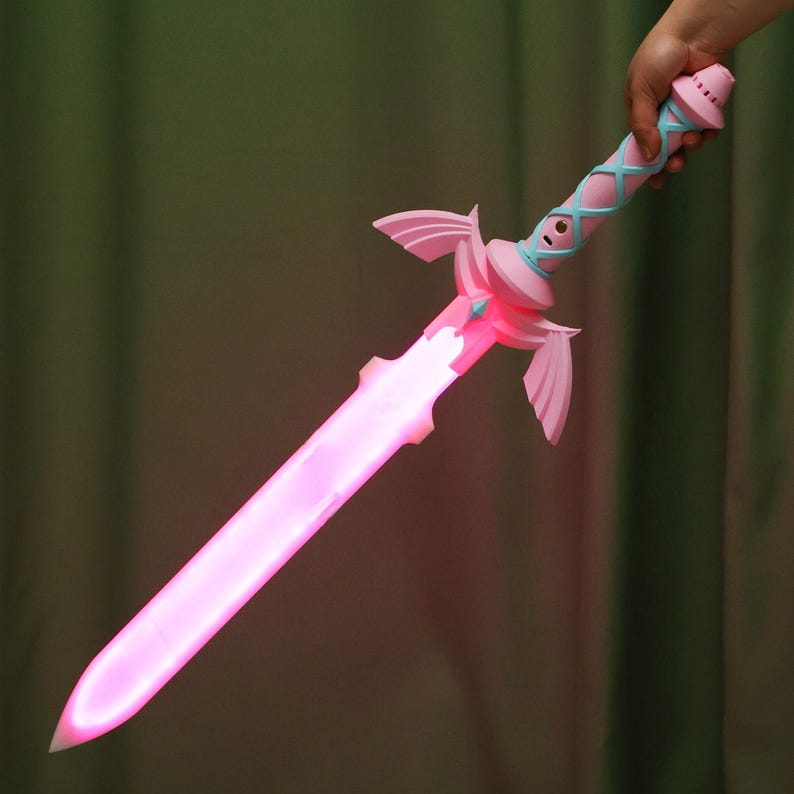 Puede incluir: Una espada de juguete de pl&aacute;stico rosa y azul con una funci&oacute;n de iluminaci&oacute;n. La espada brilla en rosa.