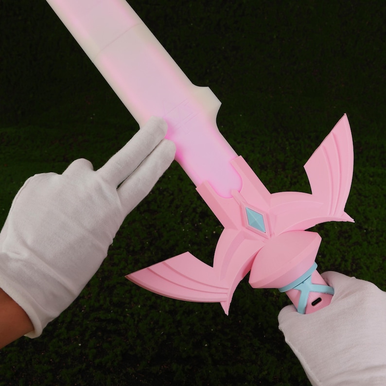 Puede incluir: Una espada de pl&aacute;stico rosa con un mango azul claro y una hoja rosa brillante. La espada tiene un dise&ntilde;o decorativo en la empu&ntilde;adura y una gran guarda en forma de ala.