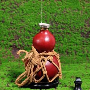 Puede incluir: Una calabaza roja con una cuerda envuelta alrededor, utilizada como fuente de agua decorativa. El agua se vierte desde la parte superior de la calabaza hasta la inferior.