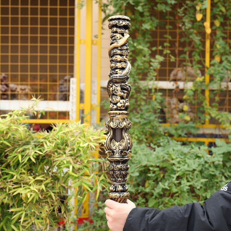 May include: A tall, ornate, carved wooden pole with a dragon motif. The pole is primarily dark brown with gold accents, featuring detailed carvings of dragons and clouds. The design is symmetrical and the pole is held by a person.
