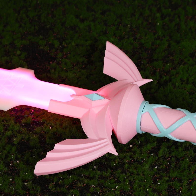 Puede incluir: Una espada de pl&aacute;stico rosa con una gema azul claro y un mango azul claro y rosa. La espada brilla en rosa.