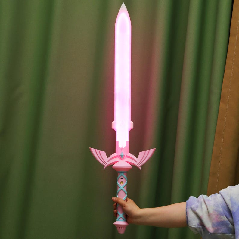 Puede incluir: Una espada de pl&aacute;stico rosa y azul con una luz rosa brillante. La espada tiene un dise&ntilde;o decorativo con alas y un mango.