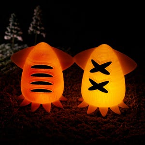 May include: Two glowing orange ceramic figurines shaped like squid with different patterns. One has a series of horizontal lines and the other has two X shapes.