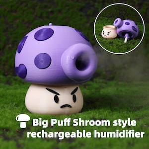 Könnte beinhalten: Ein lila-weißer, pilzförmiger, wiederaufladbarer Luftbefeuchter mit einem Cartoon-Gesicht und einer großen Düse. Der Pilzhut hat dunkelviolette Punkte. Der Text "Big Puff Shroom style rechargeable humidifier" steht unten.